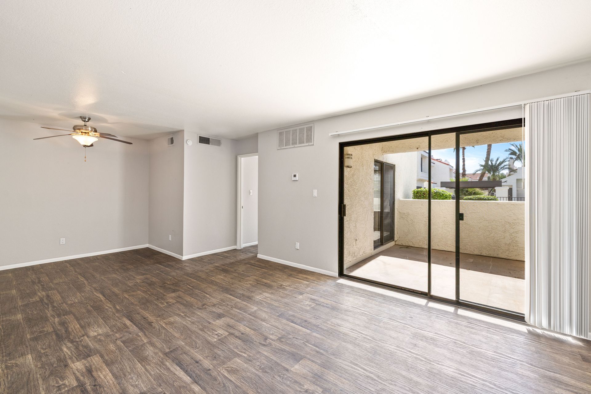 Empty living room with wood-look flooring, sliding glass door to a patio, and a ceiling fan. See why Talavera Apartments stands out among Tempe, Arizona apartments—learn more.