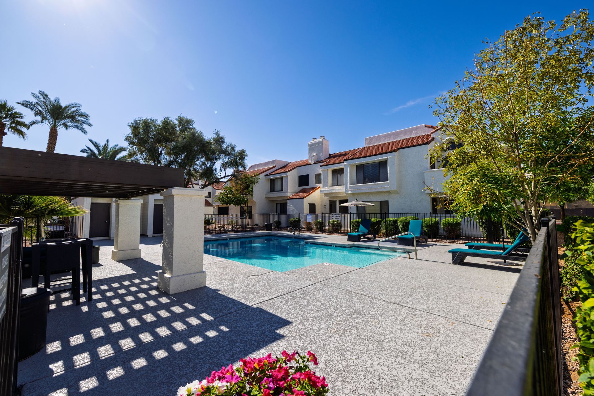 Swimming pool surrounded by a building with red tile roof, lounge chairs, and a trellis on a sunny day. Talavera Apartments offers charming pet-friendly apartments in Tempe AZ today.