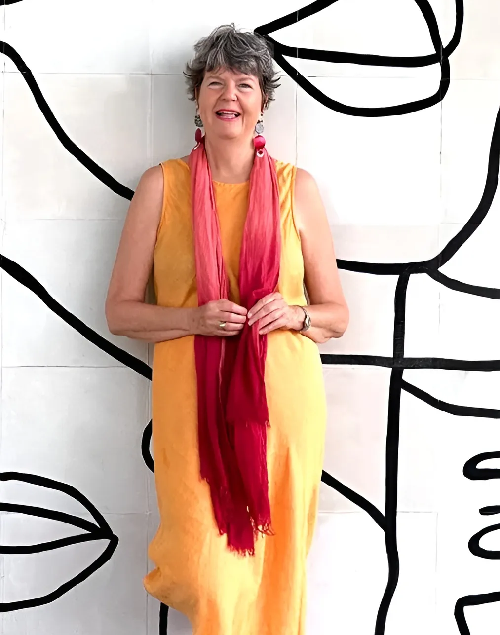 Woman in yellow dress and pink scarf standing in front of a black and white wall.