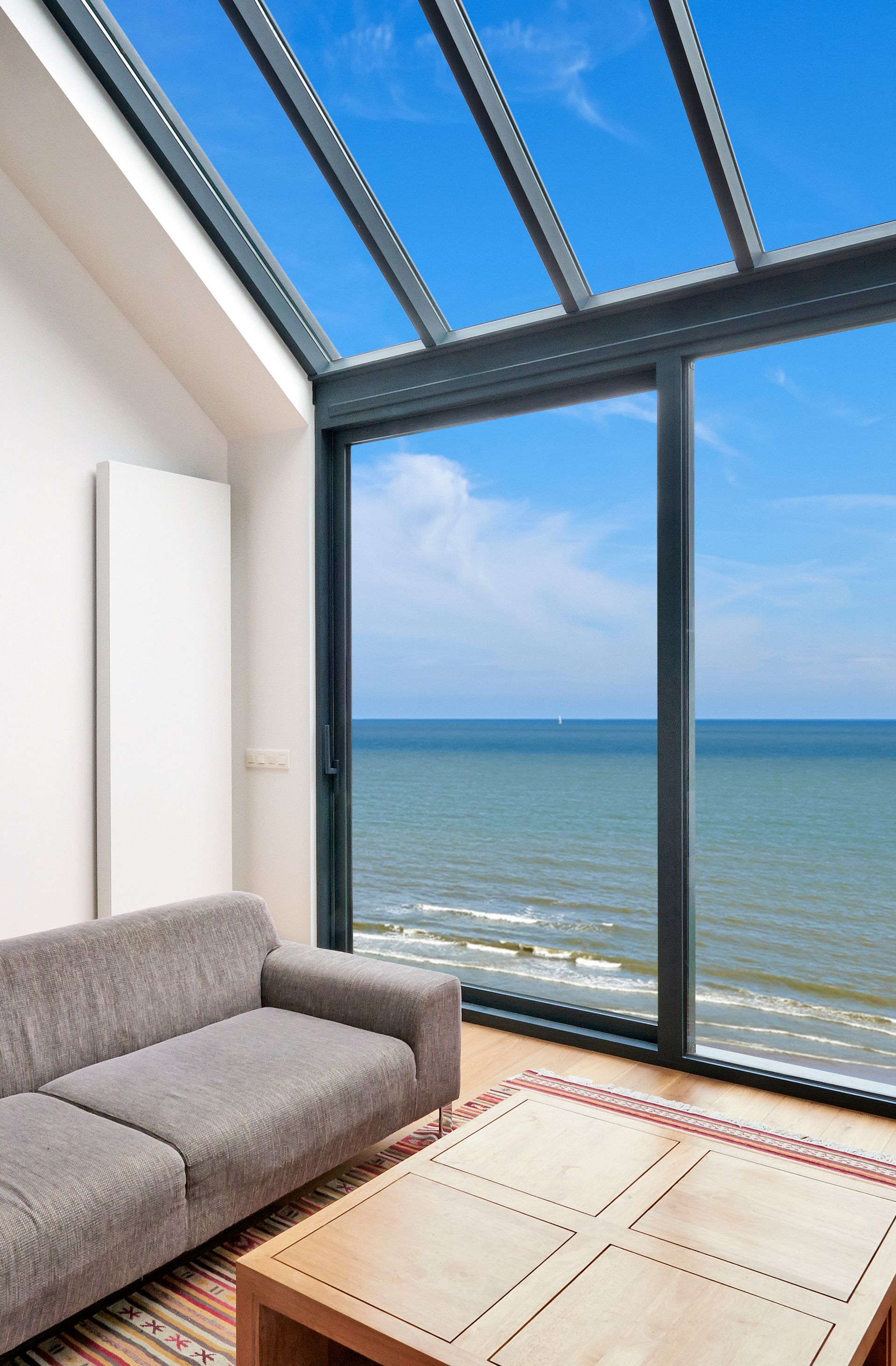 Sofa in a room with a large window and a view of the ocean and blue sky.