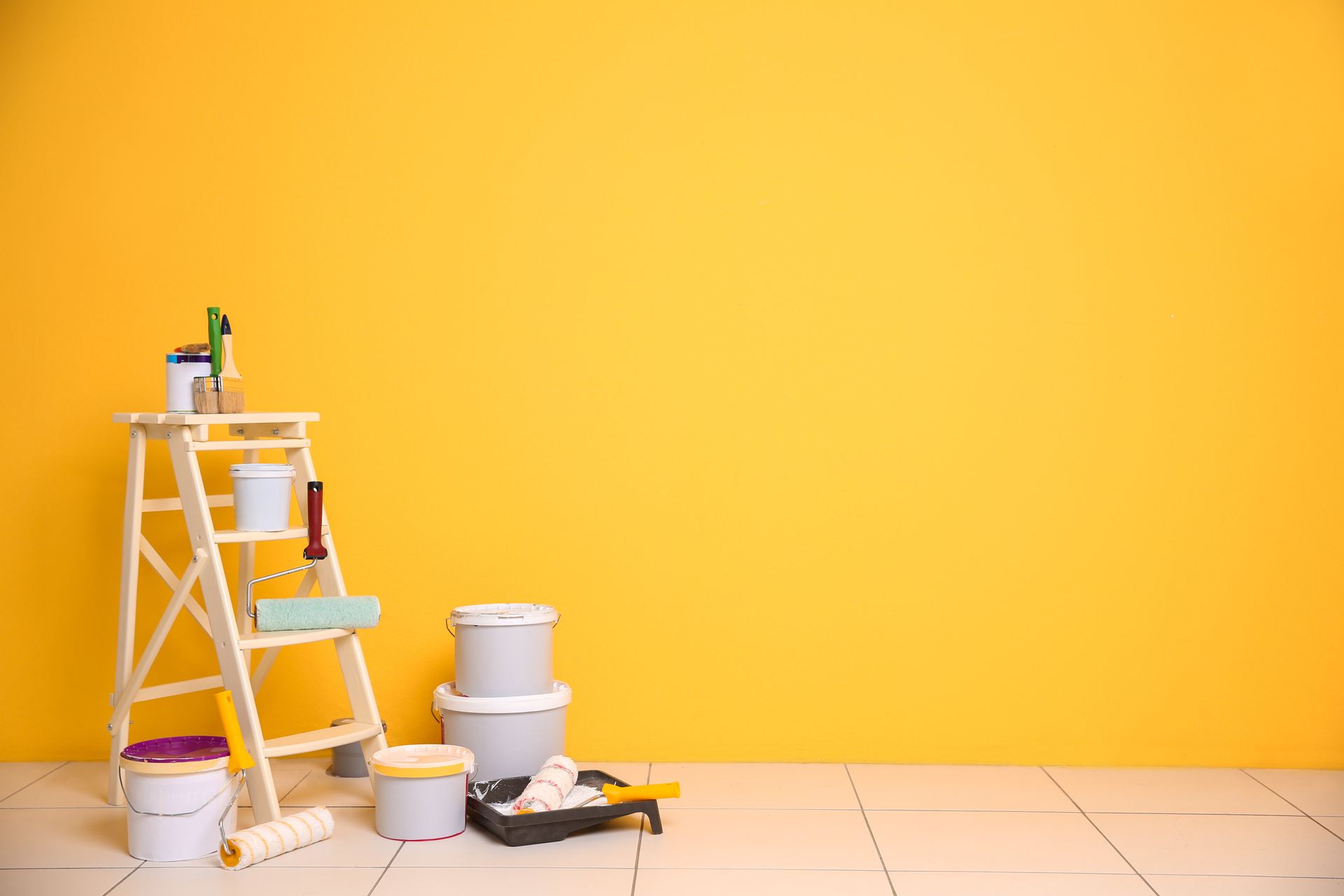Ladder with paint supplies set against a bright yellow wall.