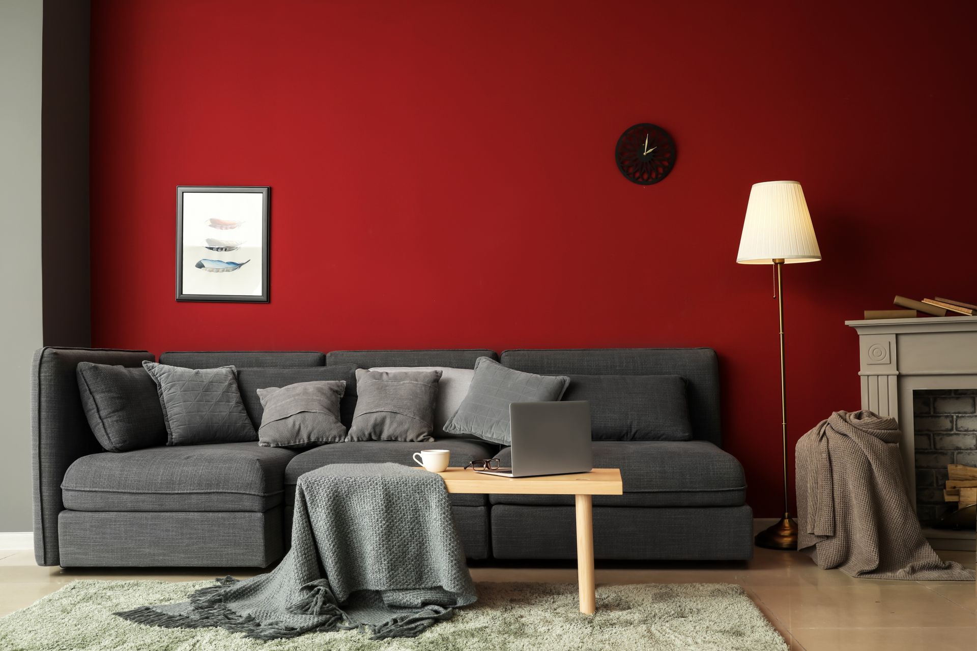 Gray sofa against a red wall with a framed picture, clock, and floor lamp in a living room.