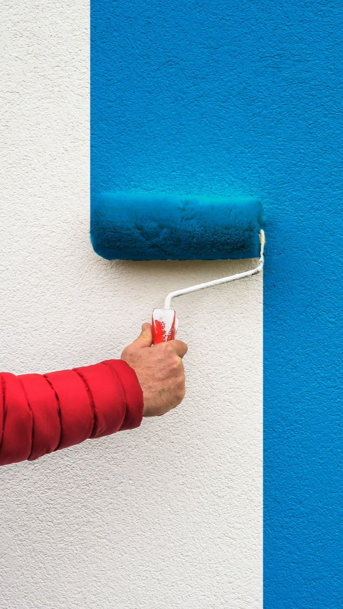 Hand painting a blue wall with a roller; a white textured wall is visible on the left.