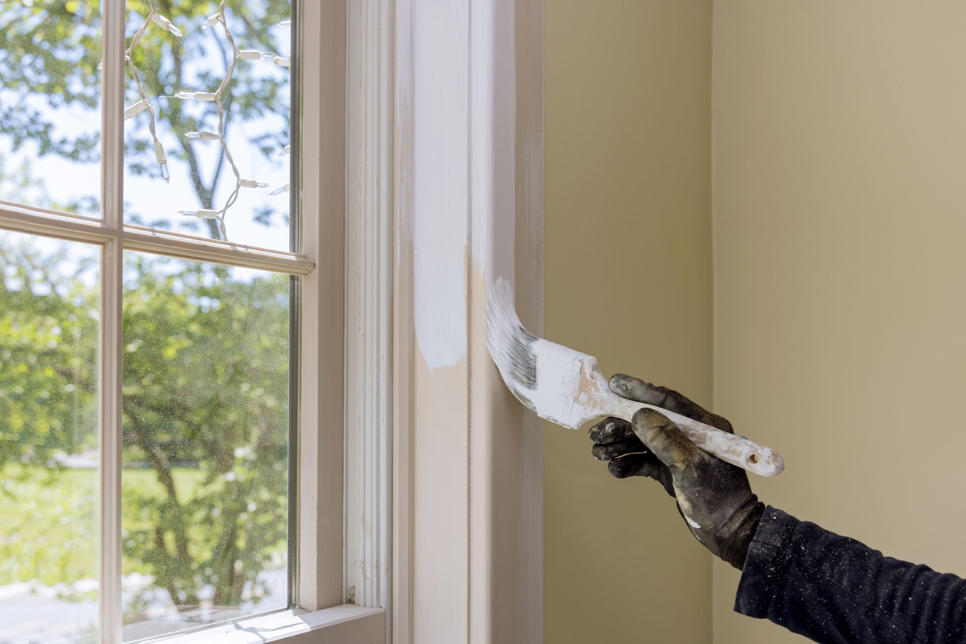 Person painting a window frame white with a brush; interior setting.