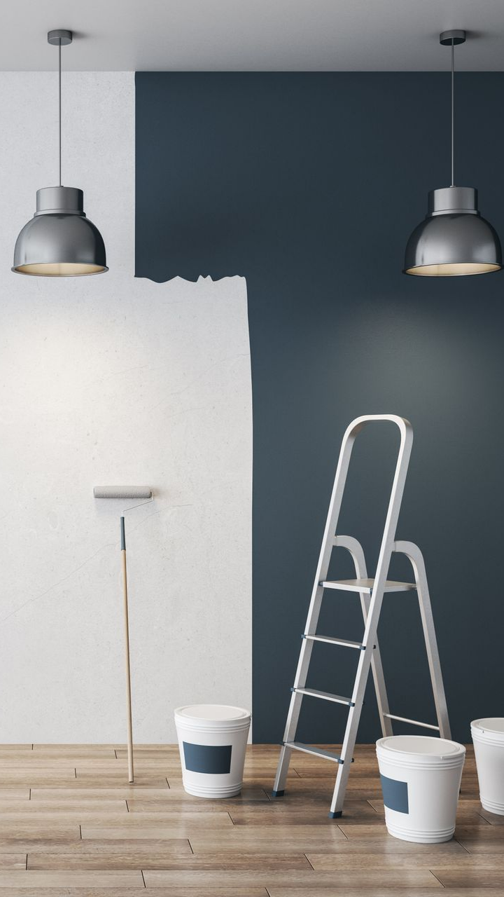 Room with white and blue walls, being painted. Paint cans, a ladder, and pendant lights.