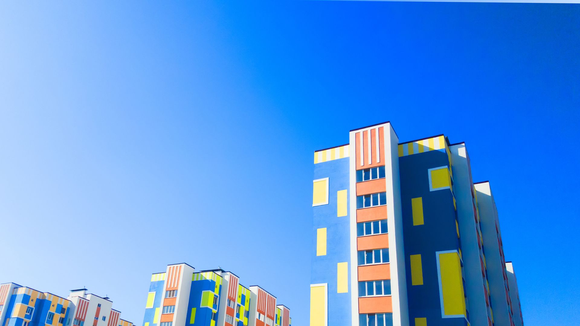 Blue and yellow multi-story apartment building against a bright blue sky.