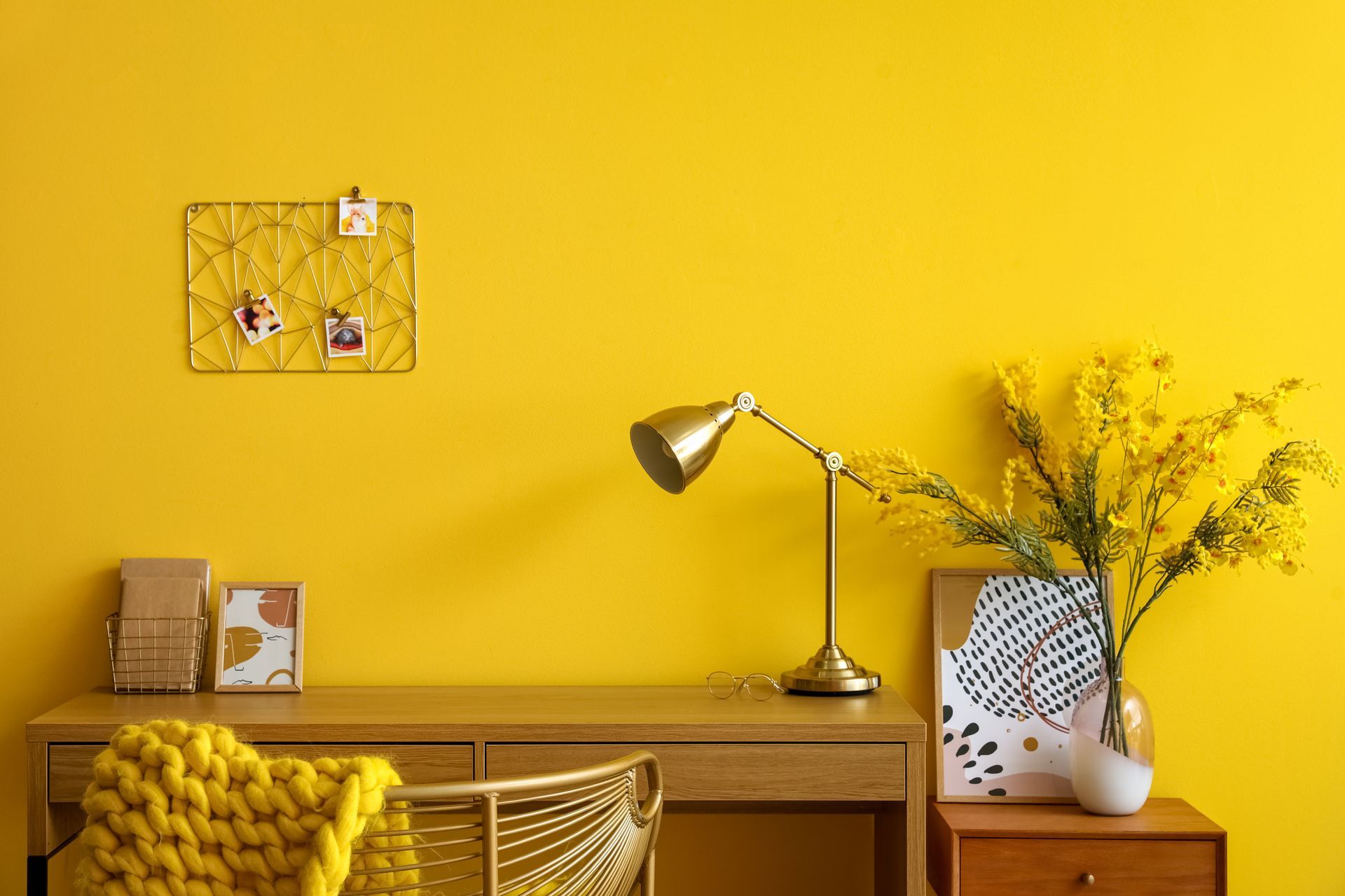 Yellow wall with desk, lamp, decor, and flowers.
