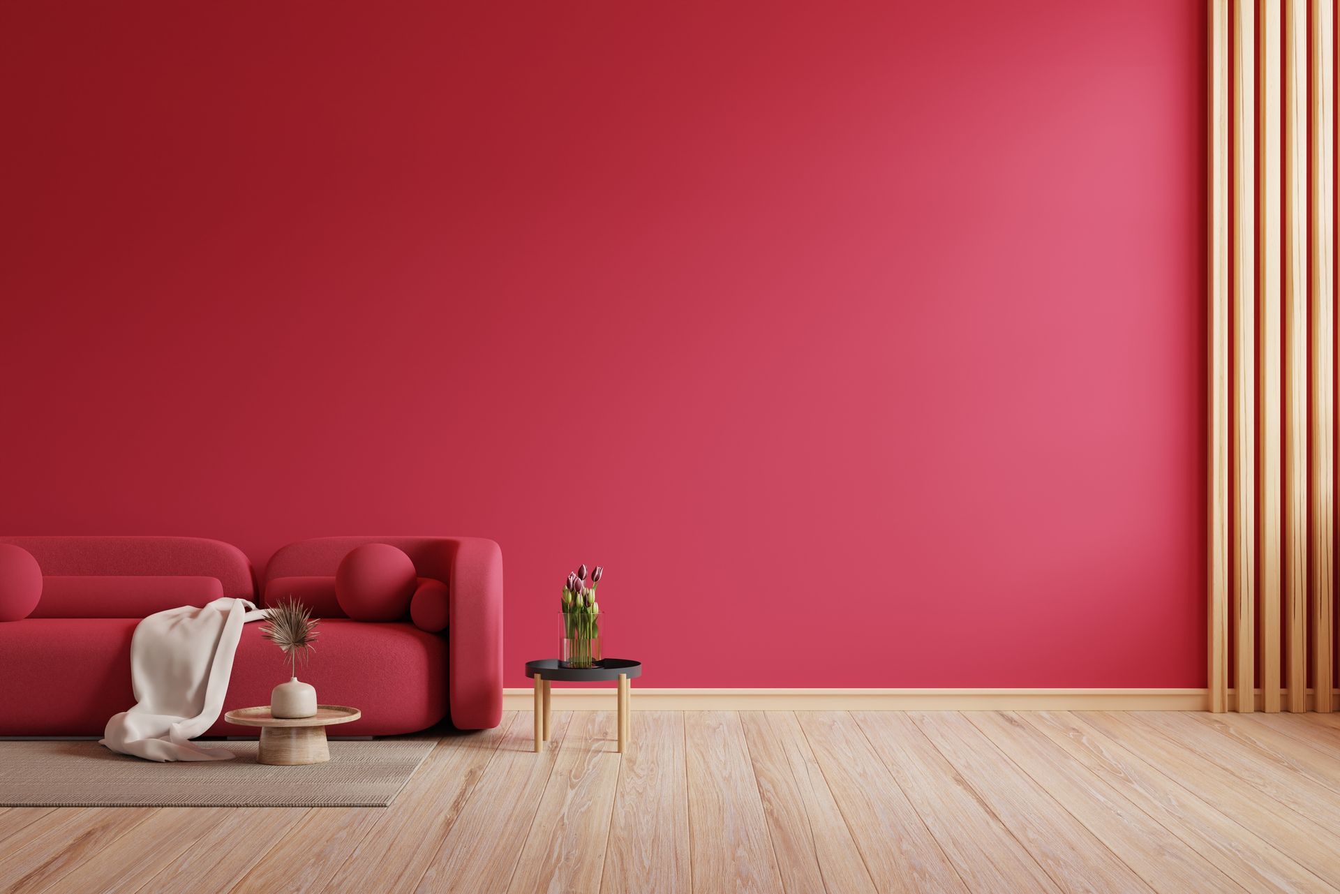 Red sofa and table against a red wall with wooden paneling and floor; a beige throw and flowers.