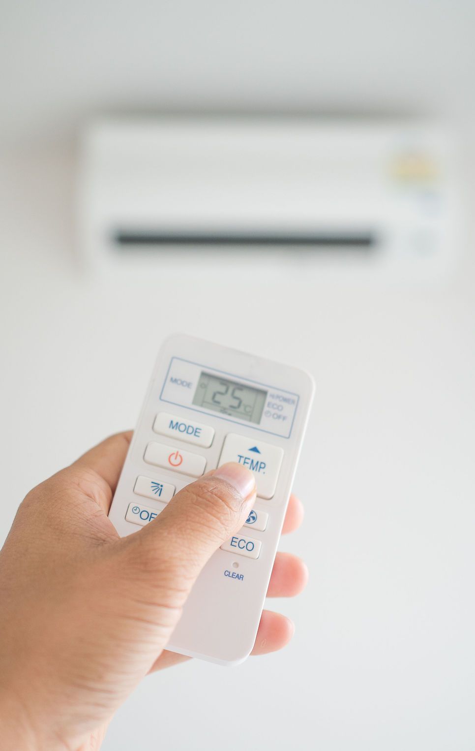 Une personne tient une télécommande devant un climatiseur.