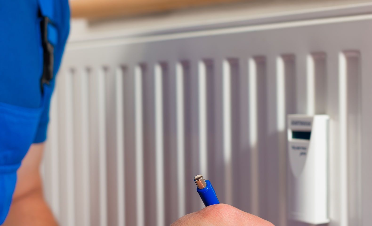 Une personne tient un crayon bleu devant un radiateur.