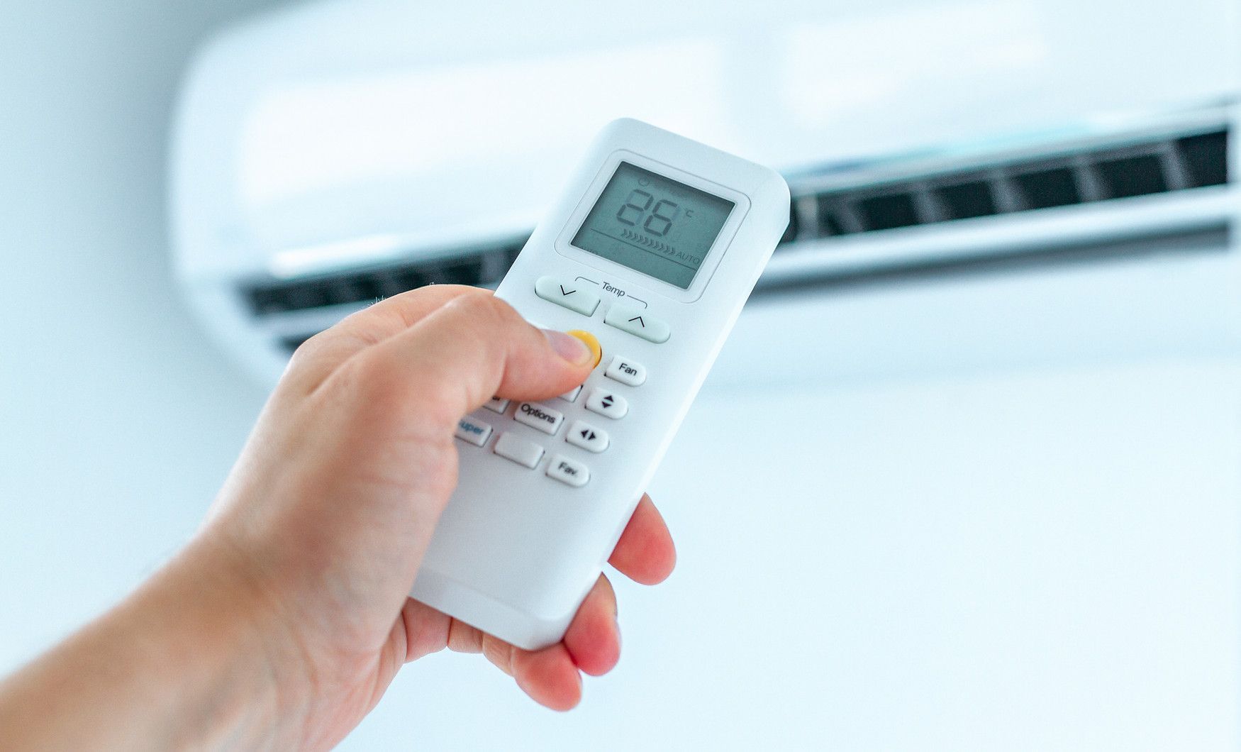 Une personne tient une télécommande devant un climatiseur.