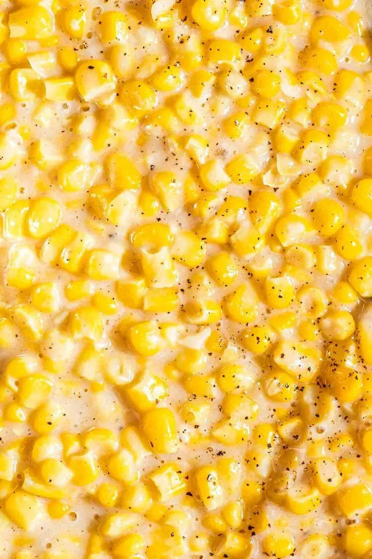 A close-up of creamy, buttery corn kernels seasoned with cracked black pepper.