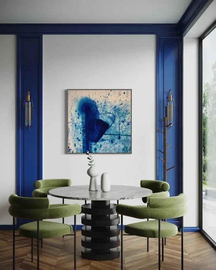 Dining room with abstract blue painting, marble table, green chairs, and blue wall trim.