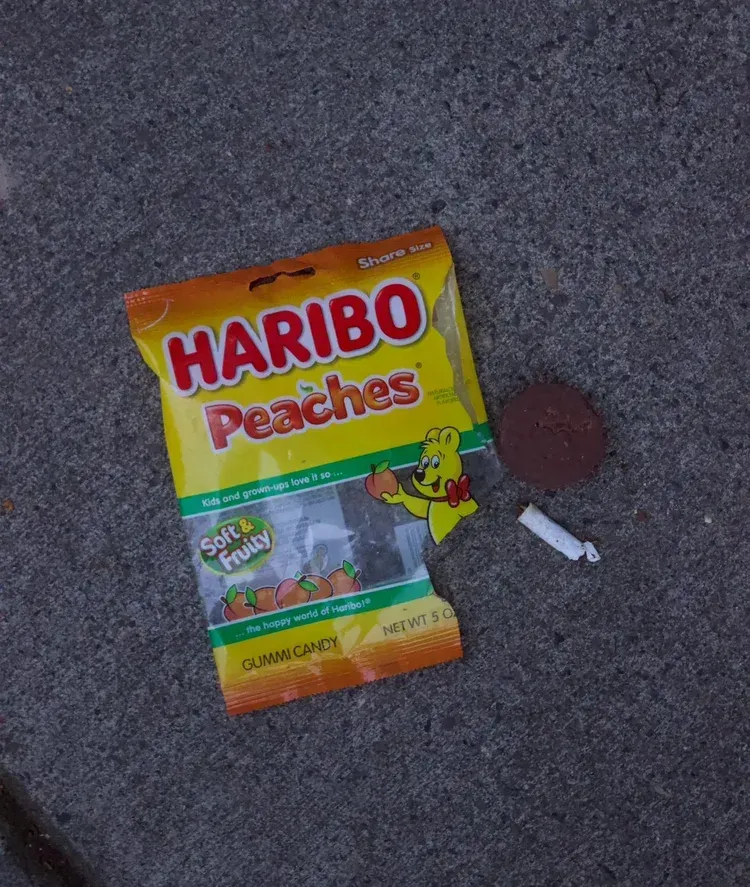 Opened bag of Haribo Peaches candy, a cookie, and a rolled paper on a gray surface.