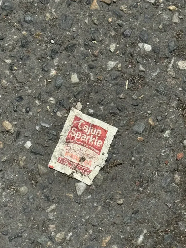 Cajun Sparkle spice packet litter on asphalt. Red and white colors.