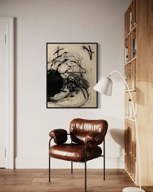Brown leather armchair, abstract art, floor lamp, and wooden bookshelf in a minimalist living room.