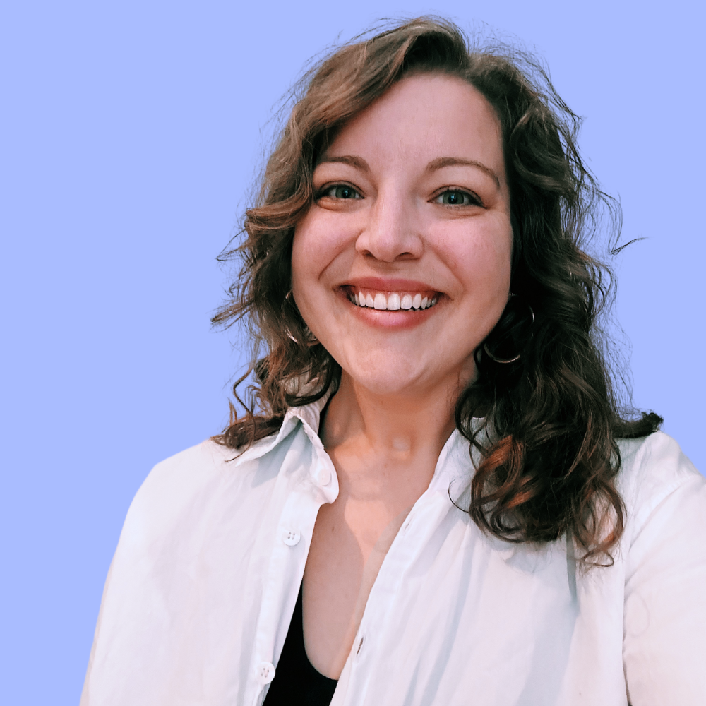 Woman with curly brown hair smiles broadly, wearing a white shirt and hoop earrings.