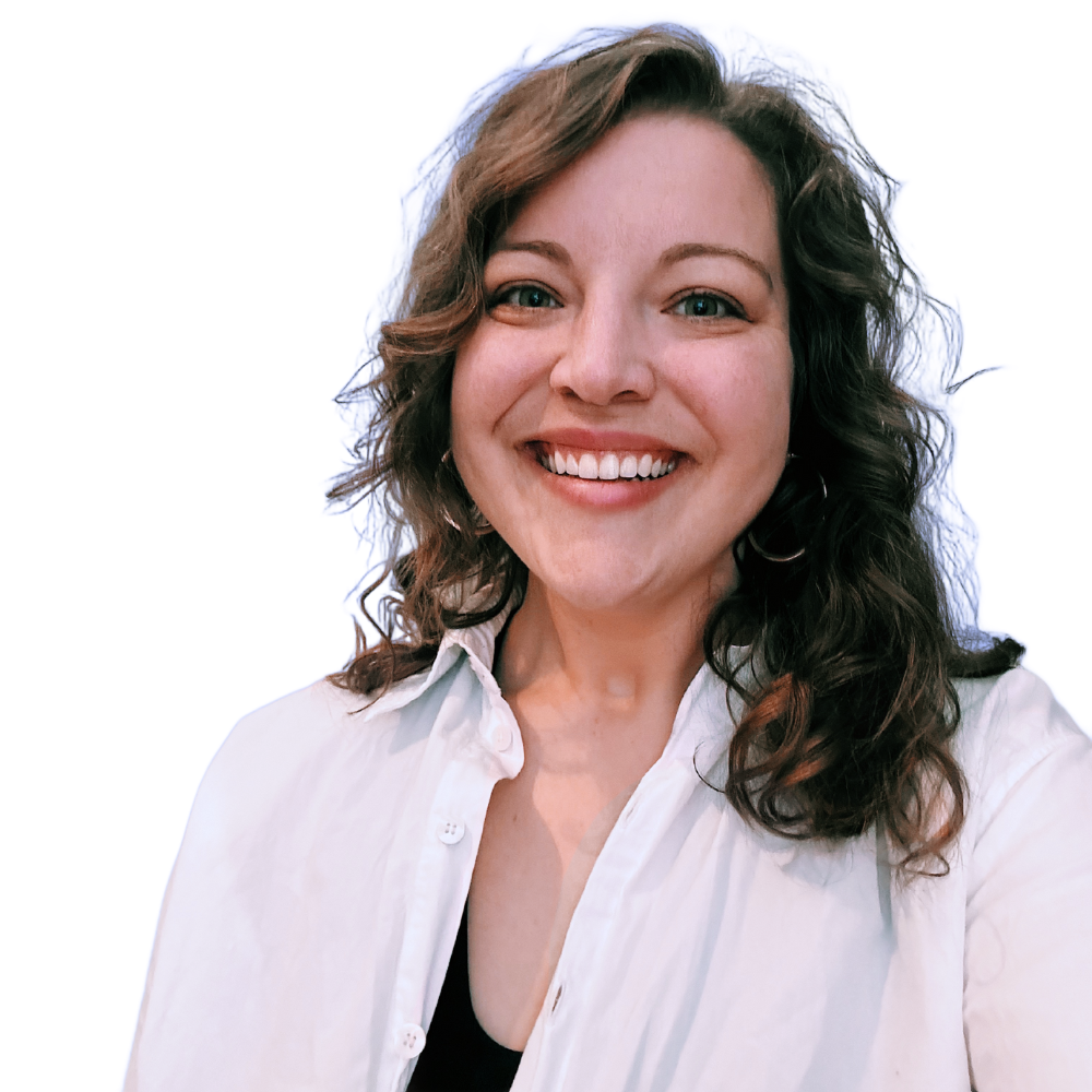 A person with shoulder-length, curly brown hair smiling at the camera, wearing a white button-down shirt over a black top.