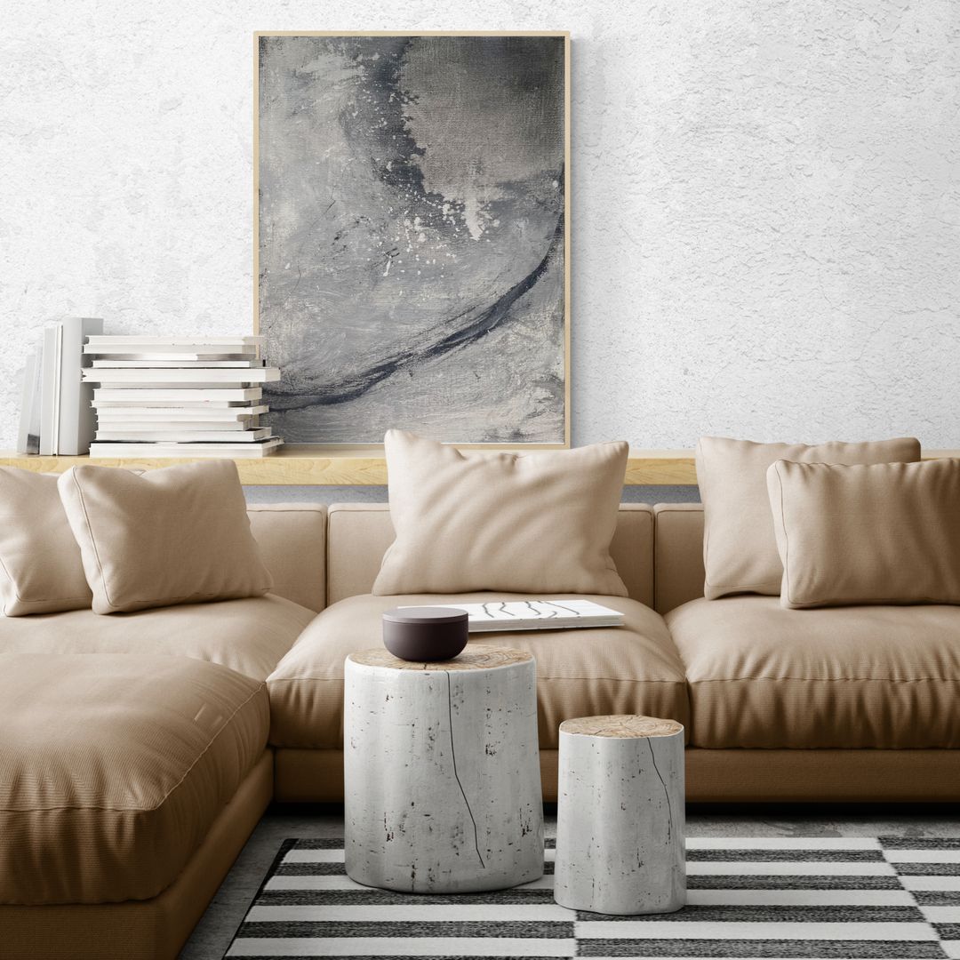 Beige sectional sofa with art, books, and striped rug. Two concrete side tables.