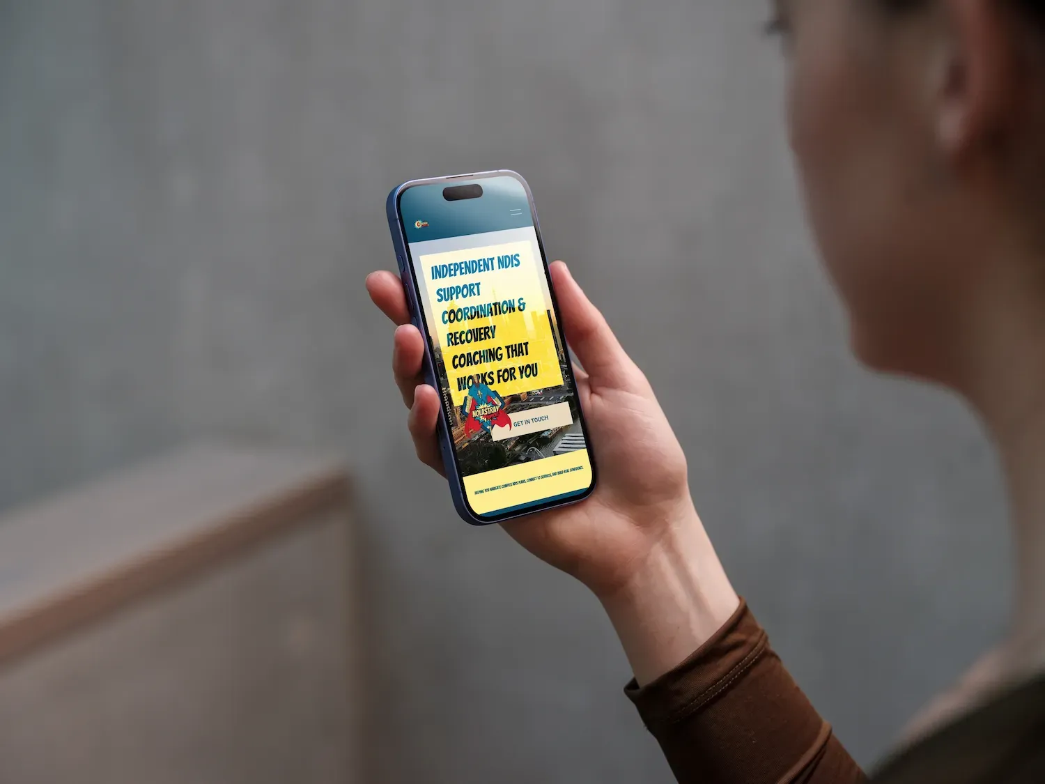 A person holding a smartphone displaying an app with text, an illustration of figures, and a yellow background.
