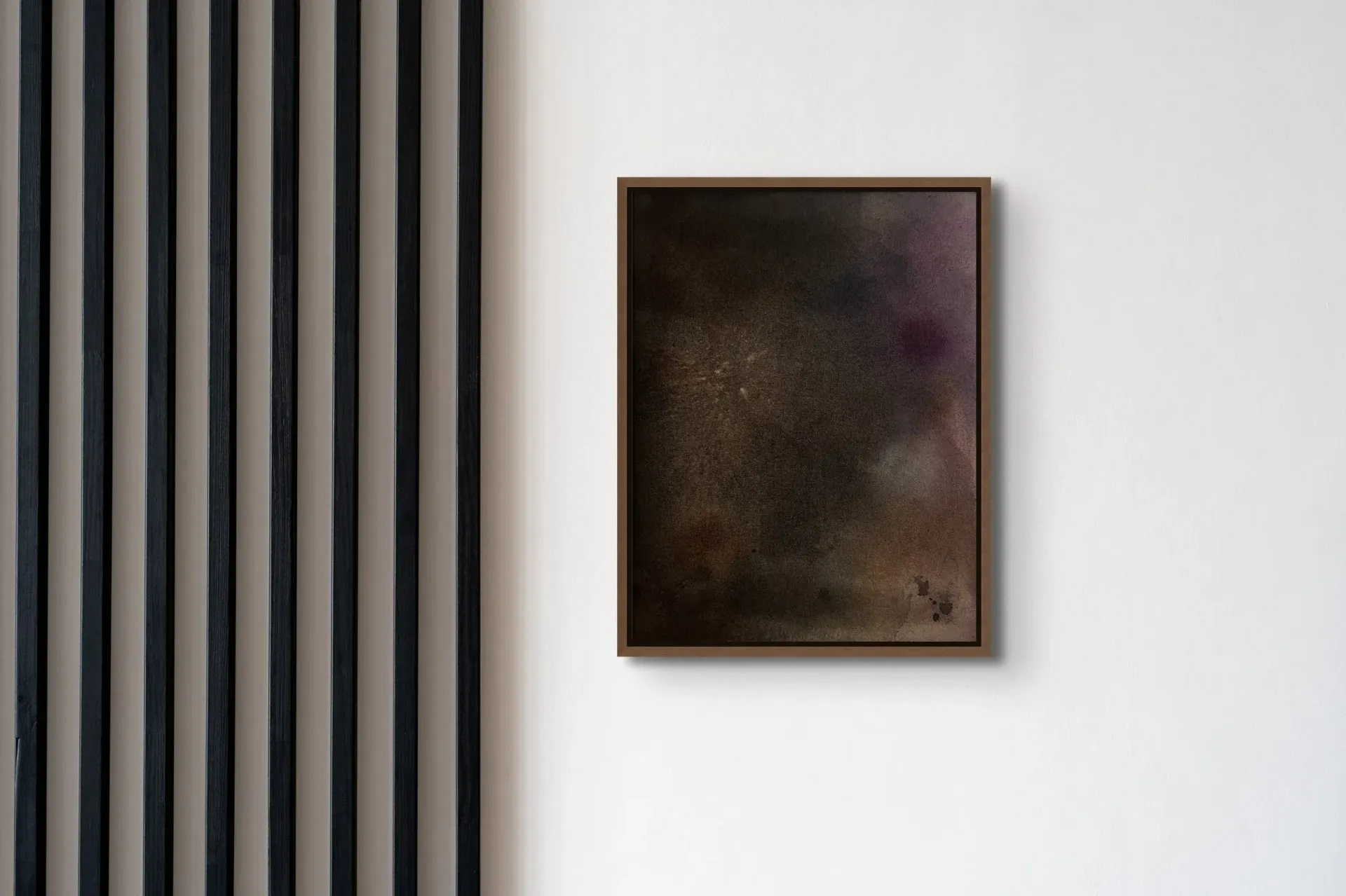 Abstract art in a brown frame on a white wall, next to black vertical wooden slats.