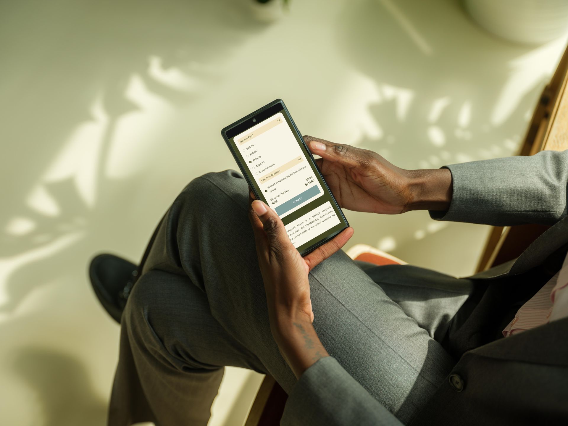 Person in a suit holding a smartphone, seated. Screen displays text and a button. Natural light.