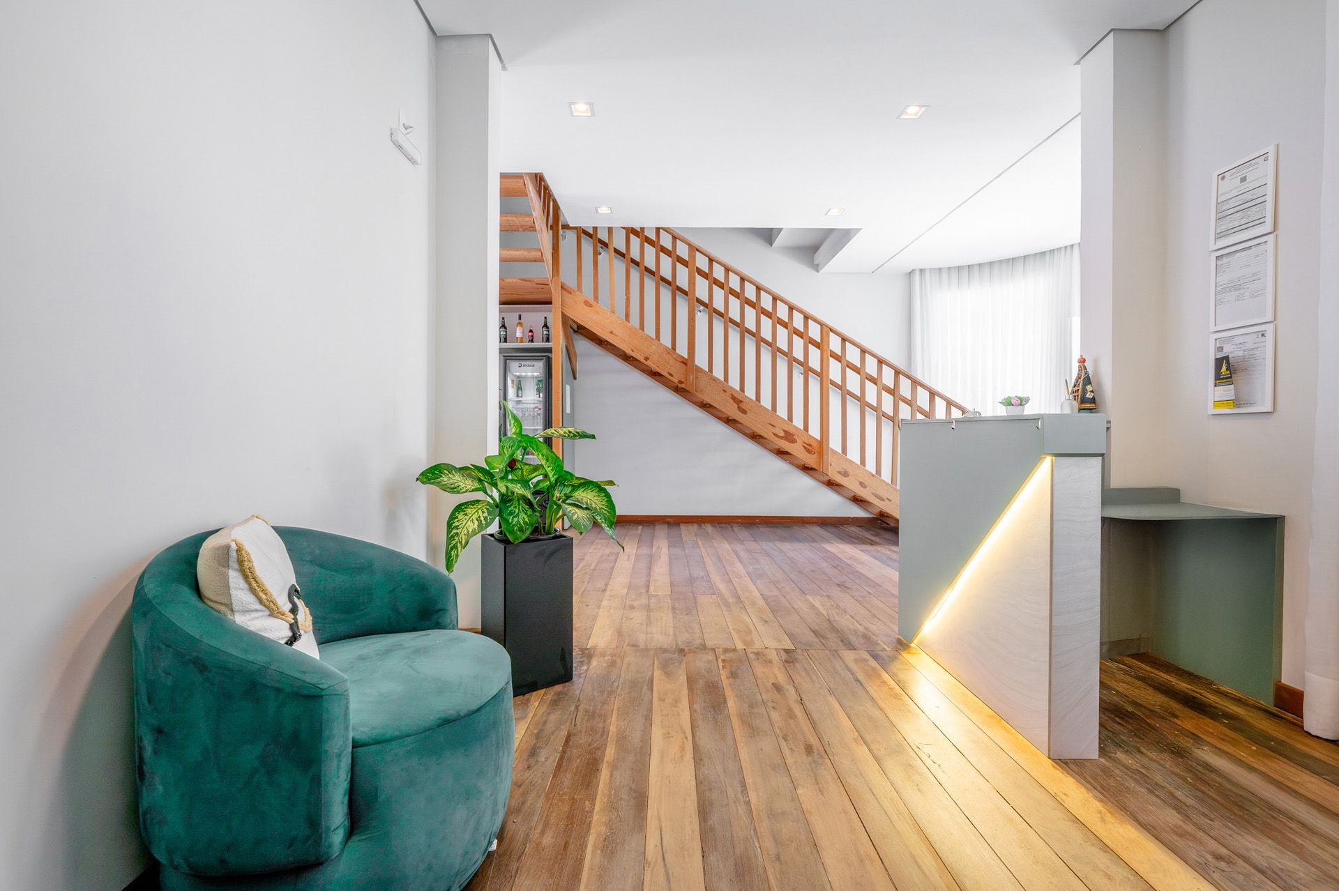 Poltrona verde, planta em vaso e escada de madeira em uma entrada moderna e iluminada com piso de madeira.