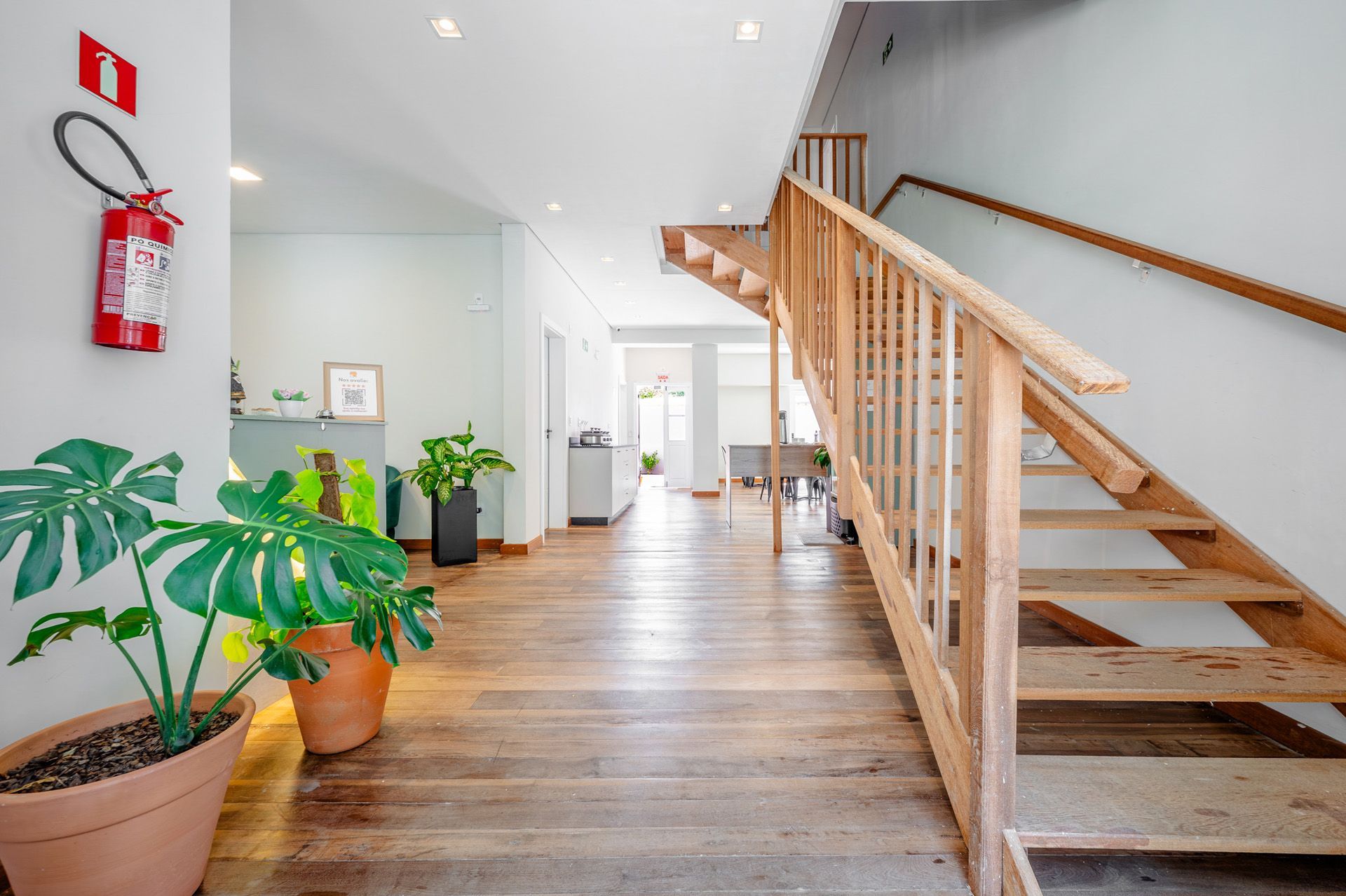 Corredor com piso e escada de madeira, vasos de plantas e extintor de incêndio.