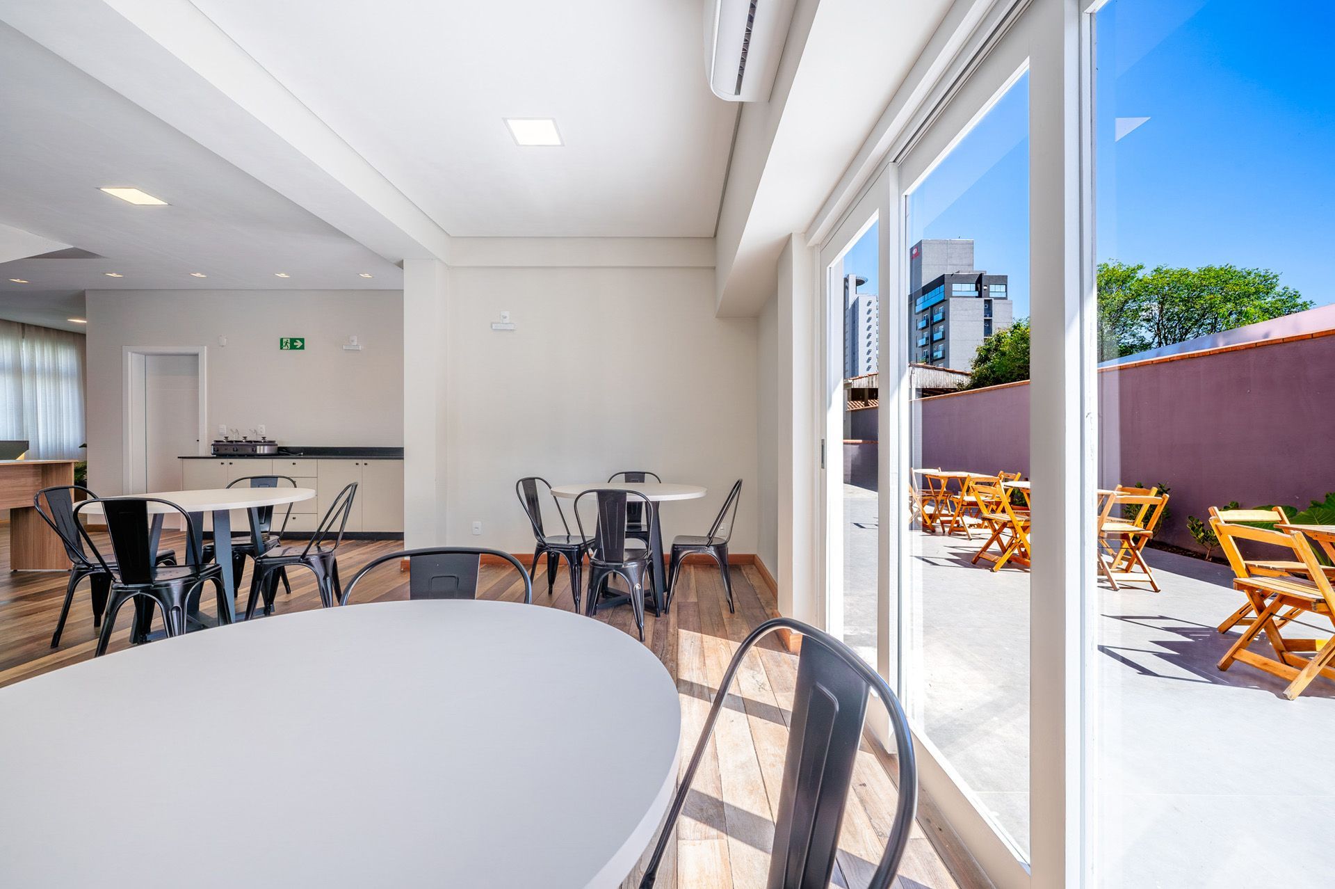 Sala interna com mesas, cadeiras e grandes portas de vidro que dão para um pátio externo com mais mesas.