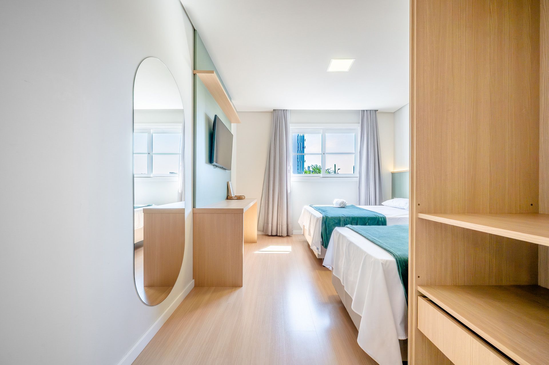 Quarto de hotel com duas camas, espelho grande e armário aberto.