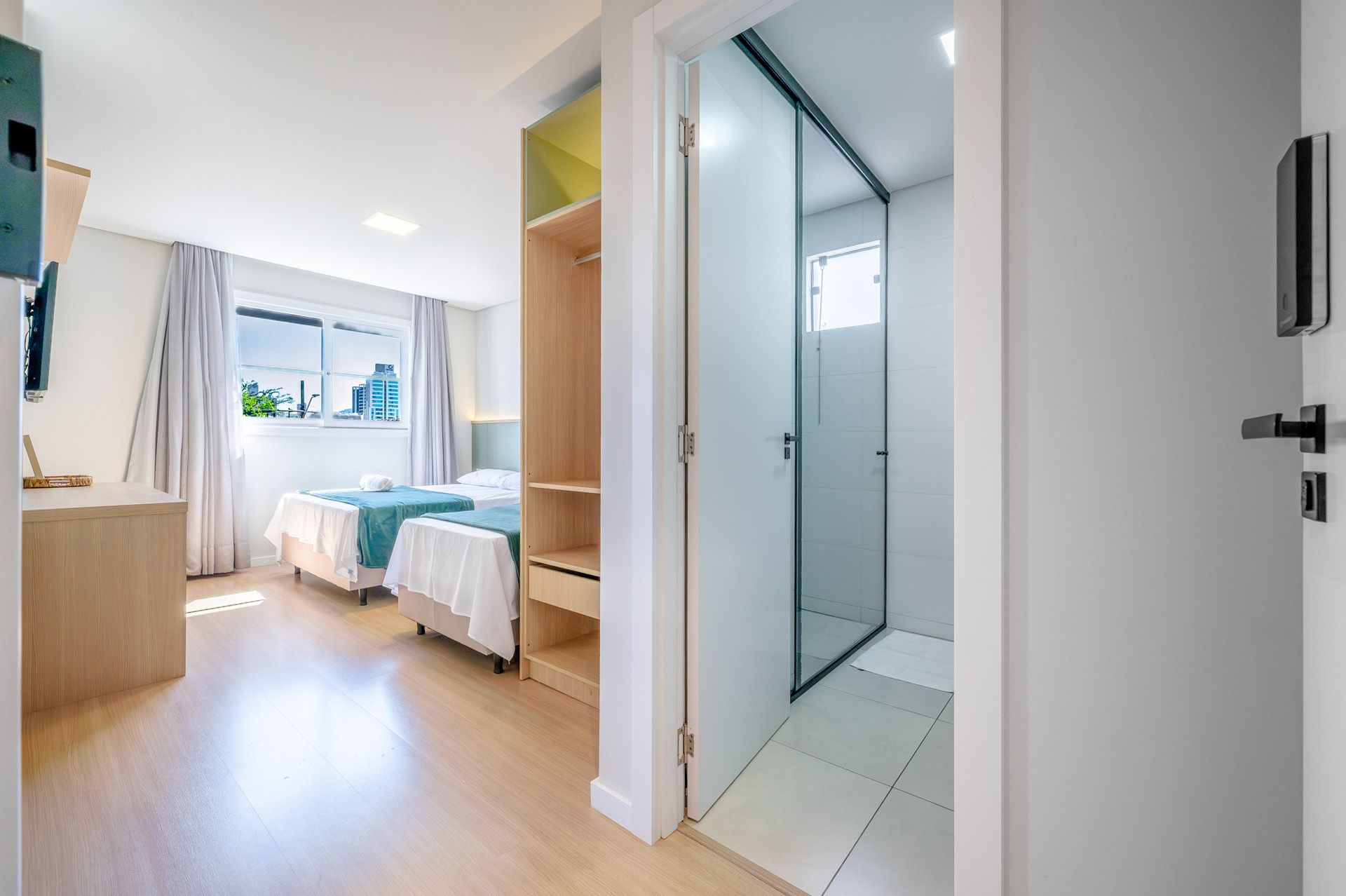 Quarto com duas camas de solteiro, armário e box de chuveiro visível.