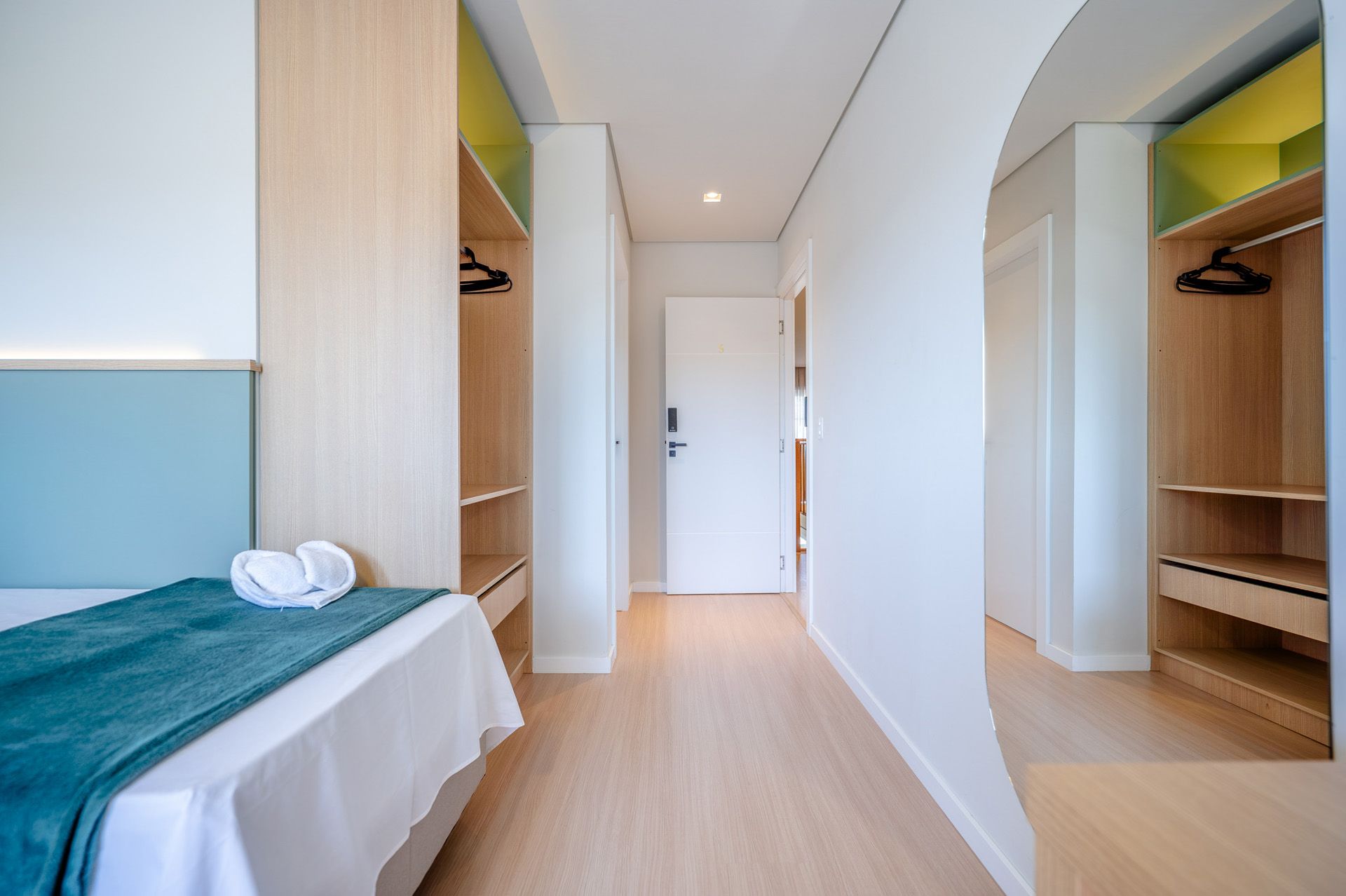 Quarto com cama, armários e corredor. Piso de madeira clara e cores neutras.