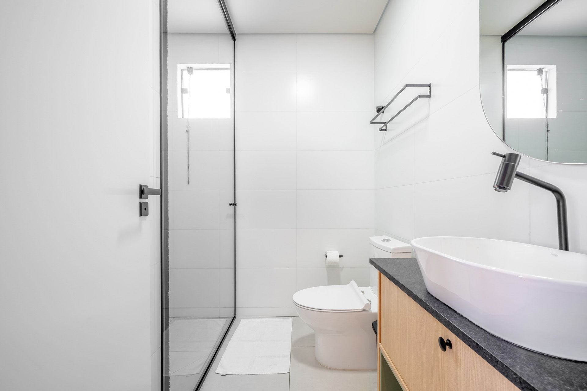 Banheiro branco com chuveiro, vaso sanitário, pia e espelho.