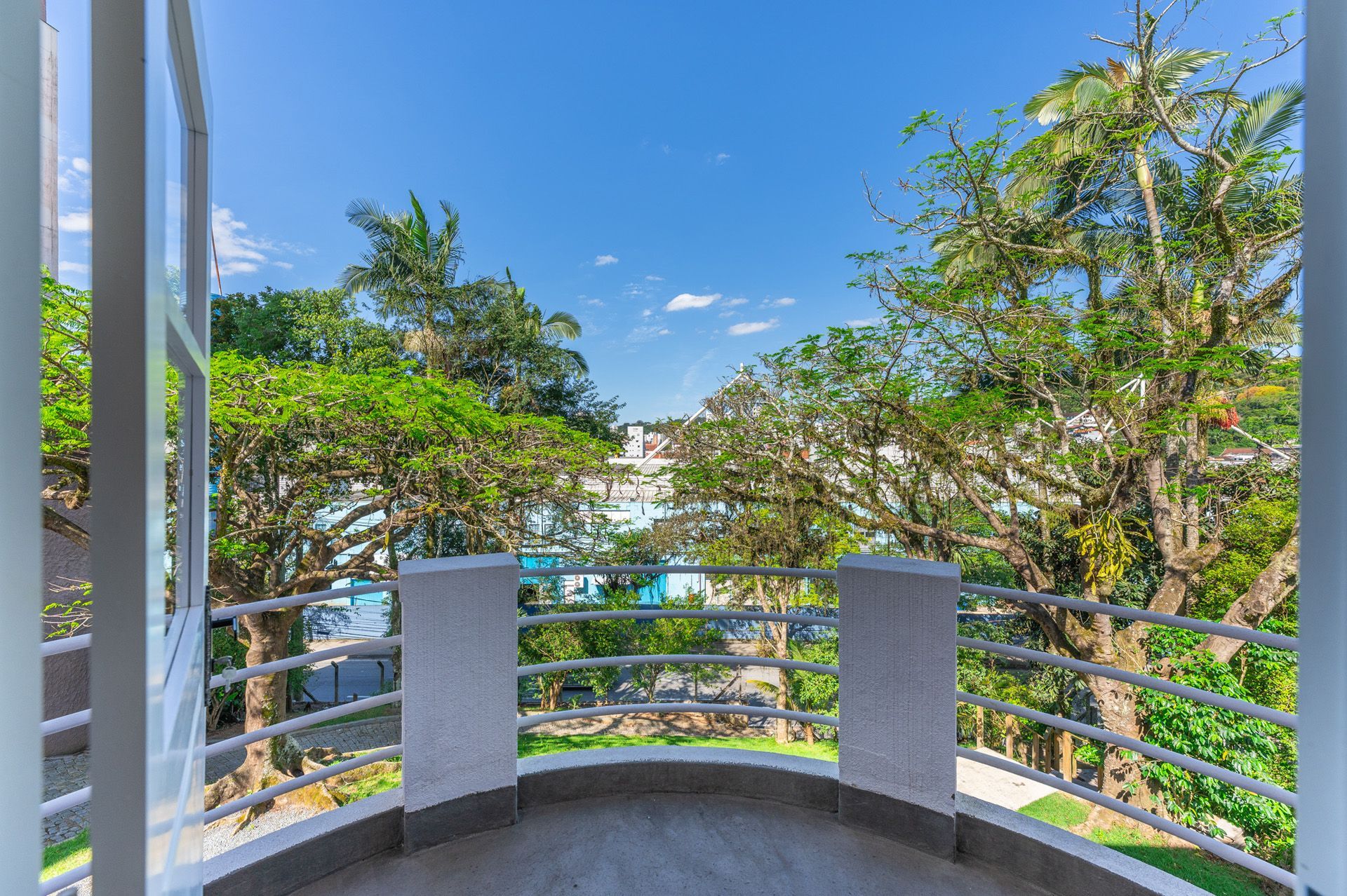 Varanda com vista para árvores e edifícios contra um céu azul.