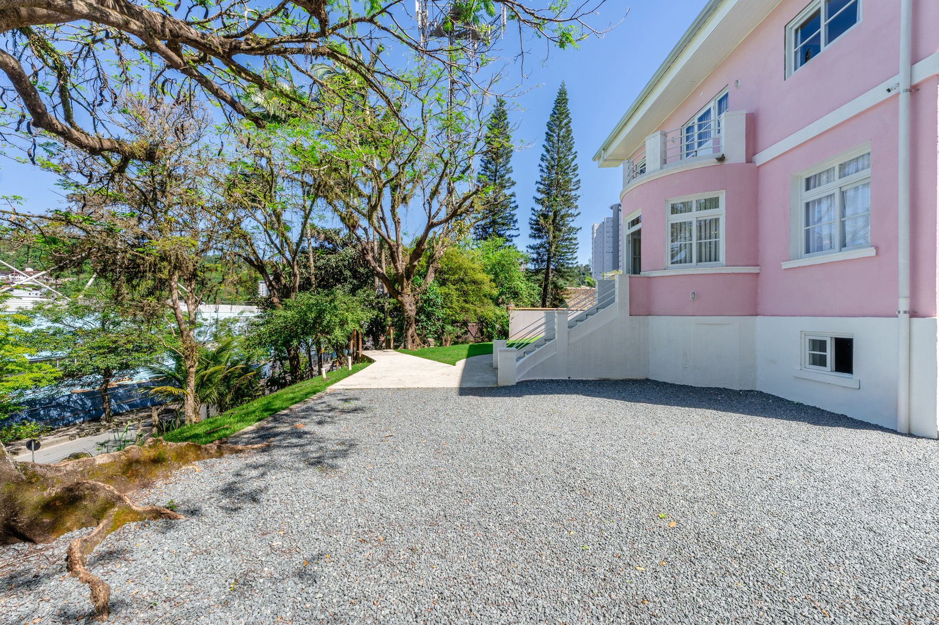 Casa rosa com entrada de cascalho e vegetação ao redor em um dia ensolarado.