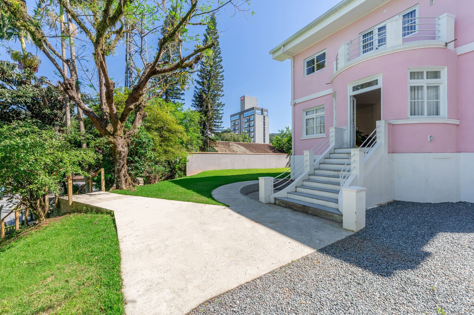 Casa rosa com detalhes em branco, entrada de automóveis com cascalho cinza e gramado verde.