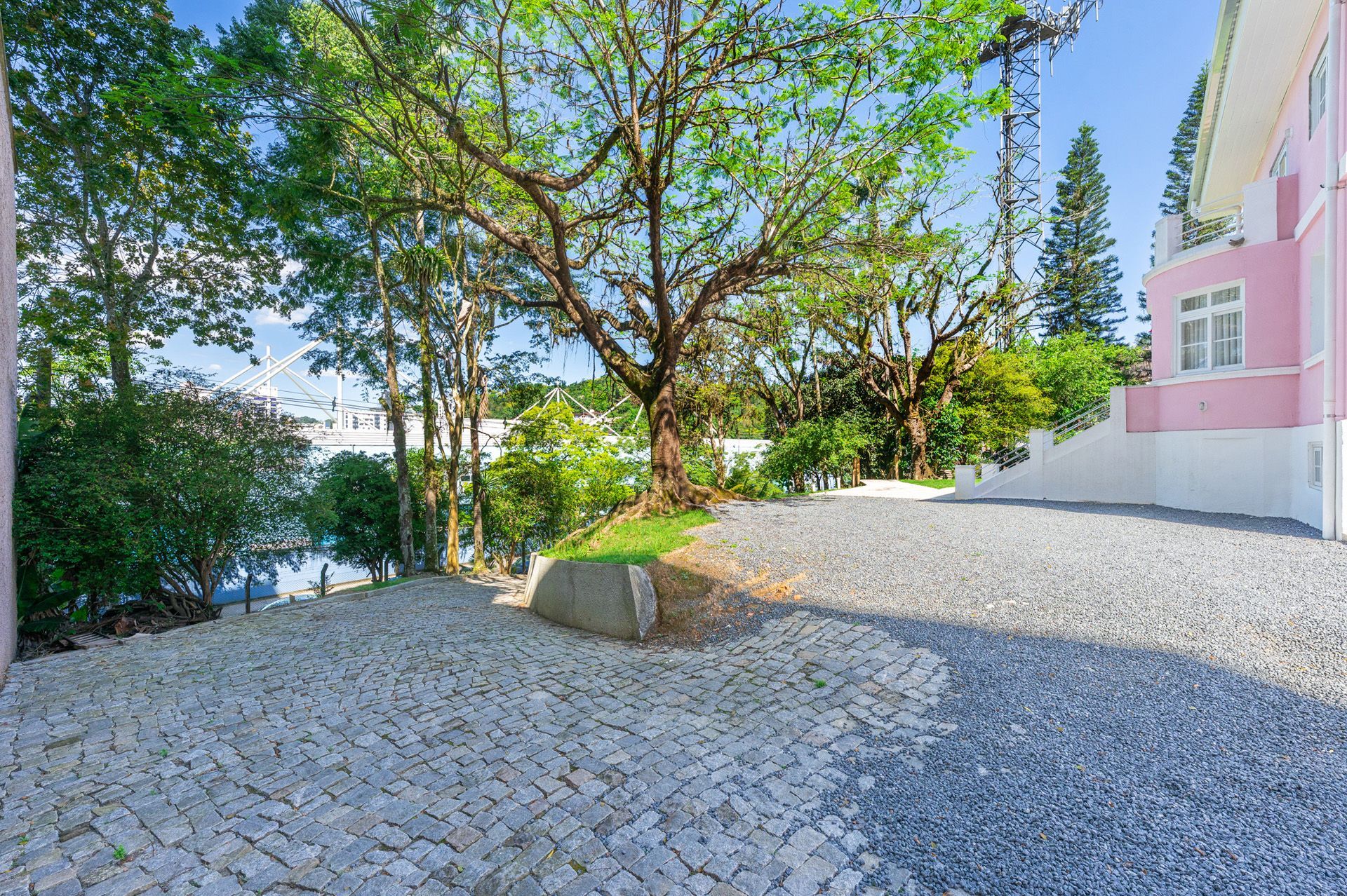 Caminho de cascalho ao lado de um prédio rosa e árvores, que leva a um corpo d'água.