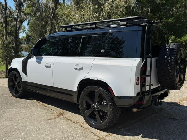 A white land rover defender is parked on the side of the road.