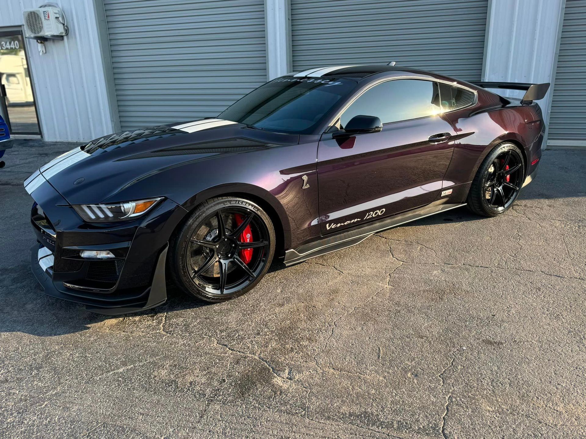 A purple ford mustang is parked in front of a garage.