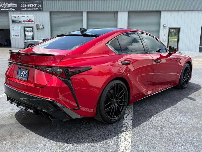 Red Lexus sedan parked outside a shop, featuring black rims and tinted windows.