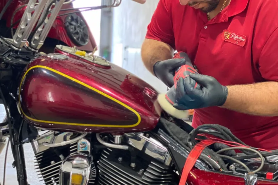 A man in a red shirt is polishing a red motorcycle.