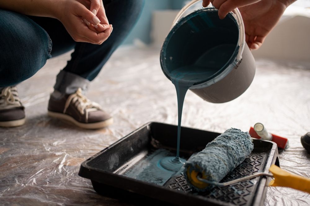 A person is pouring blue paint into a paint roller.