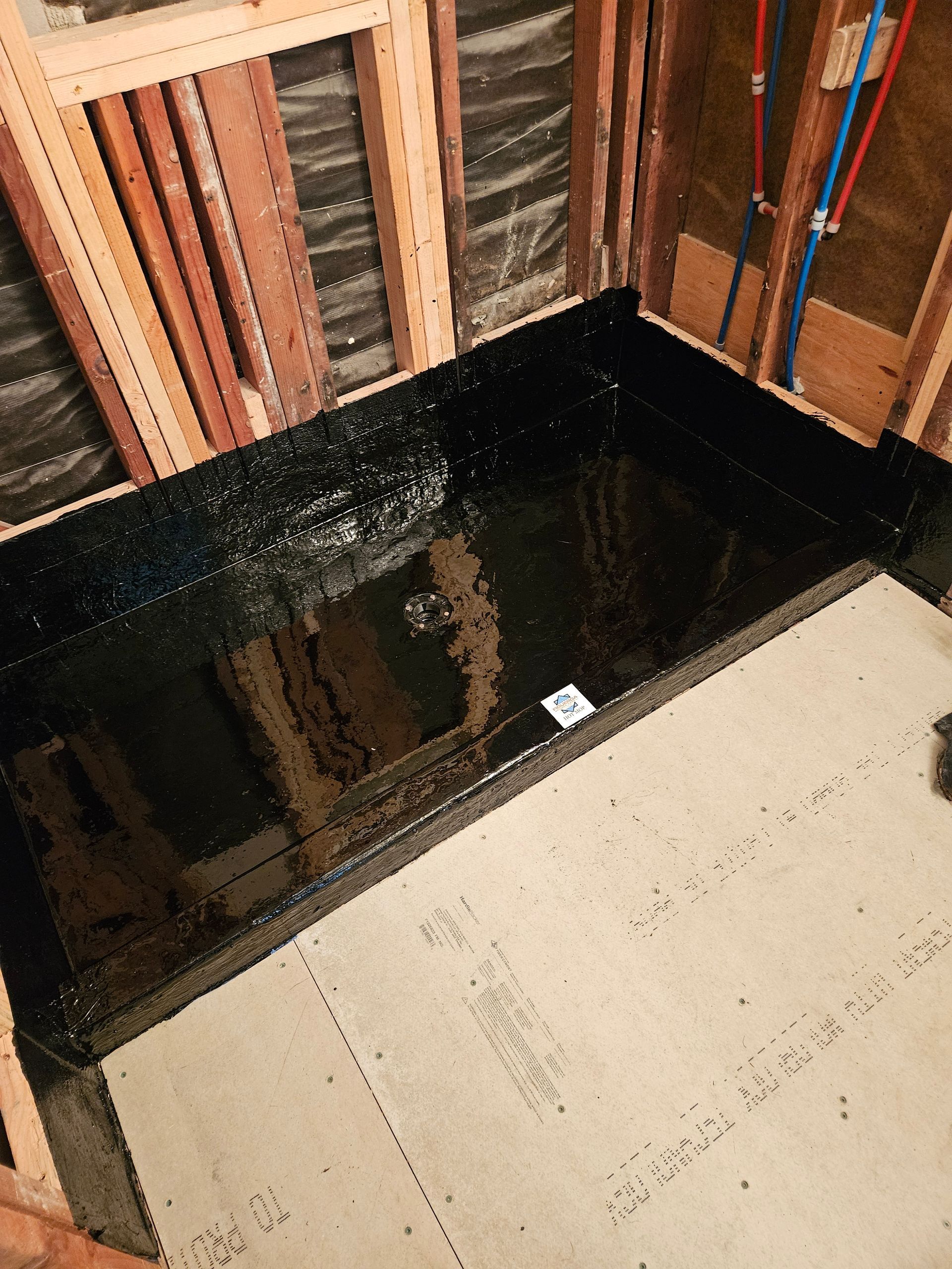 Spacious shower with beige tile walls, a pebble-covered bench, and dark fixtures. A decorative mosaic strip runs vertically.
