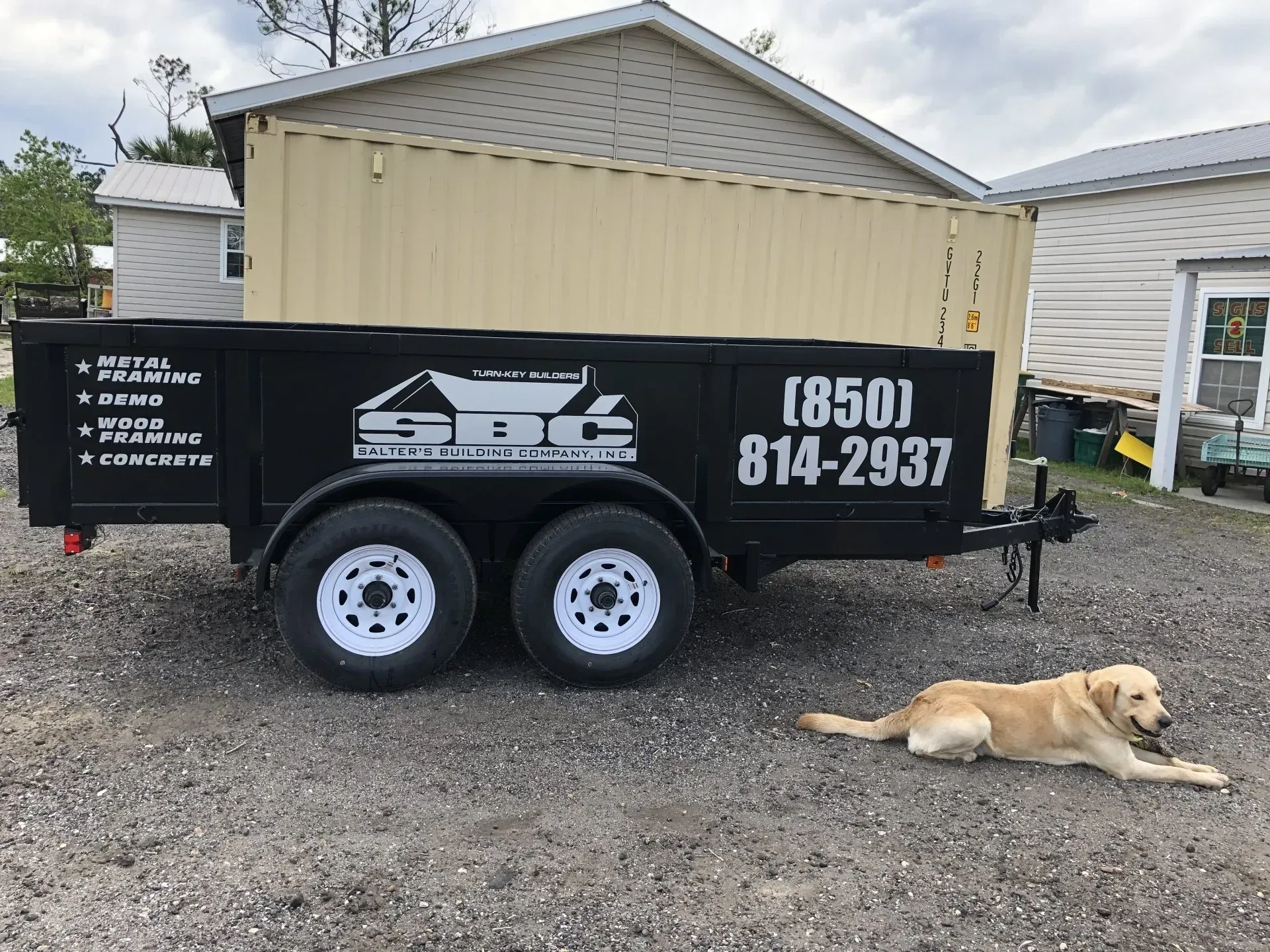 A dog is laying next to a dumpster that says sbc on it