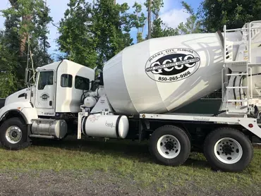 A concrete mixer truck is parked in a grassy area.