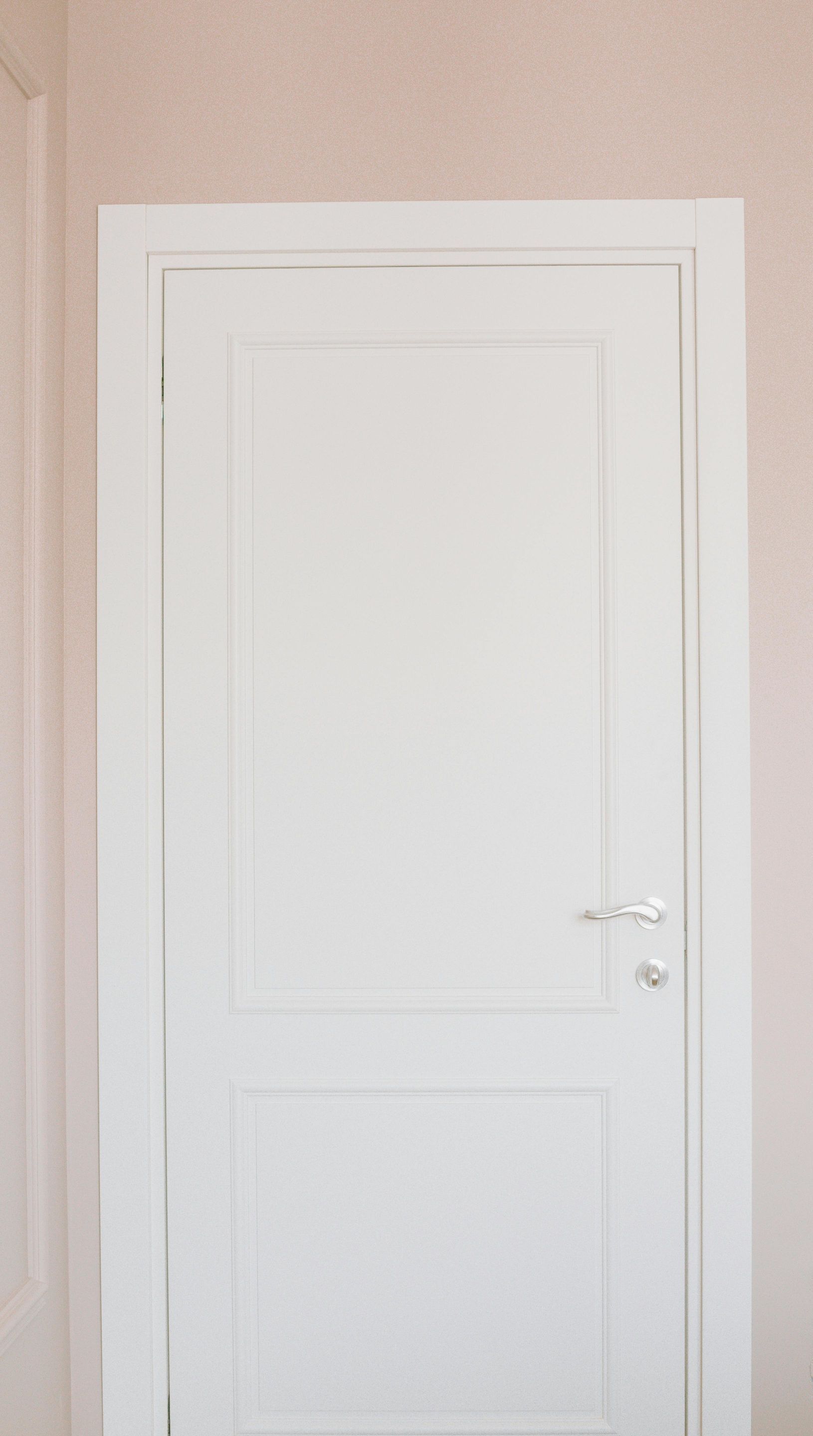A white door is against a pink wall in a room.