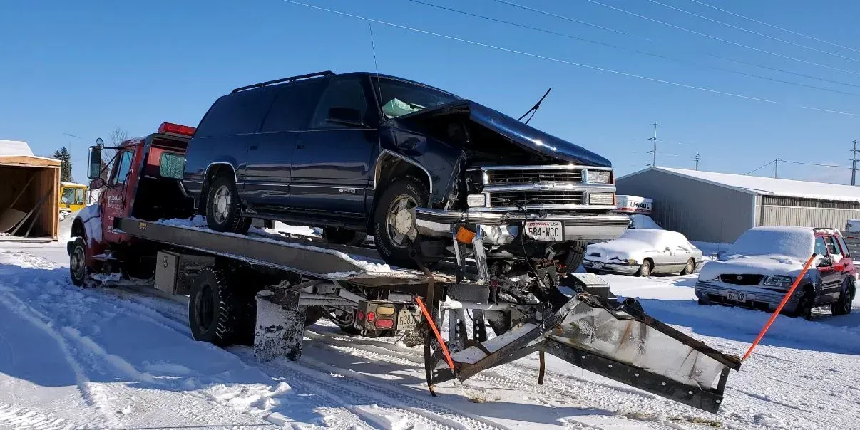 A tow truck is carrying a damaged van in the snow.