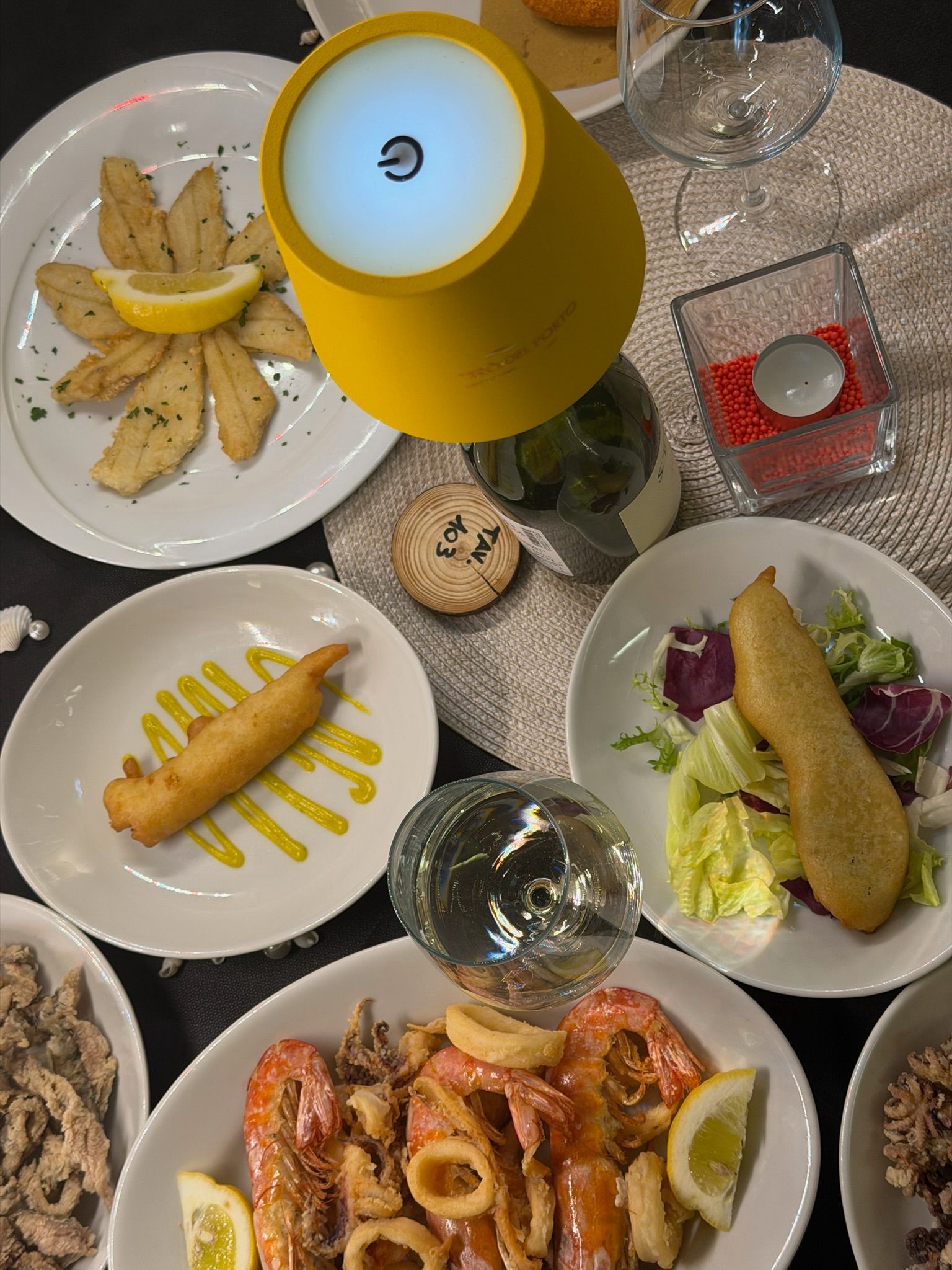 Un insieme di piatti di mare accompagnati da un bicchiere di vino e una bottiglia lampada