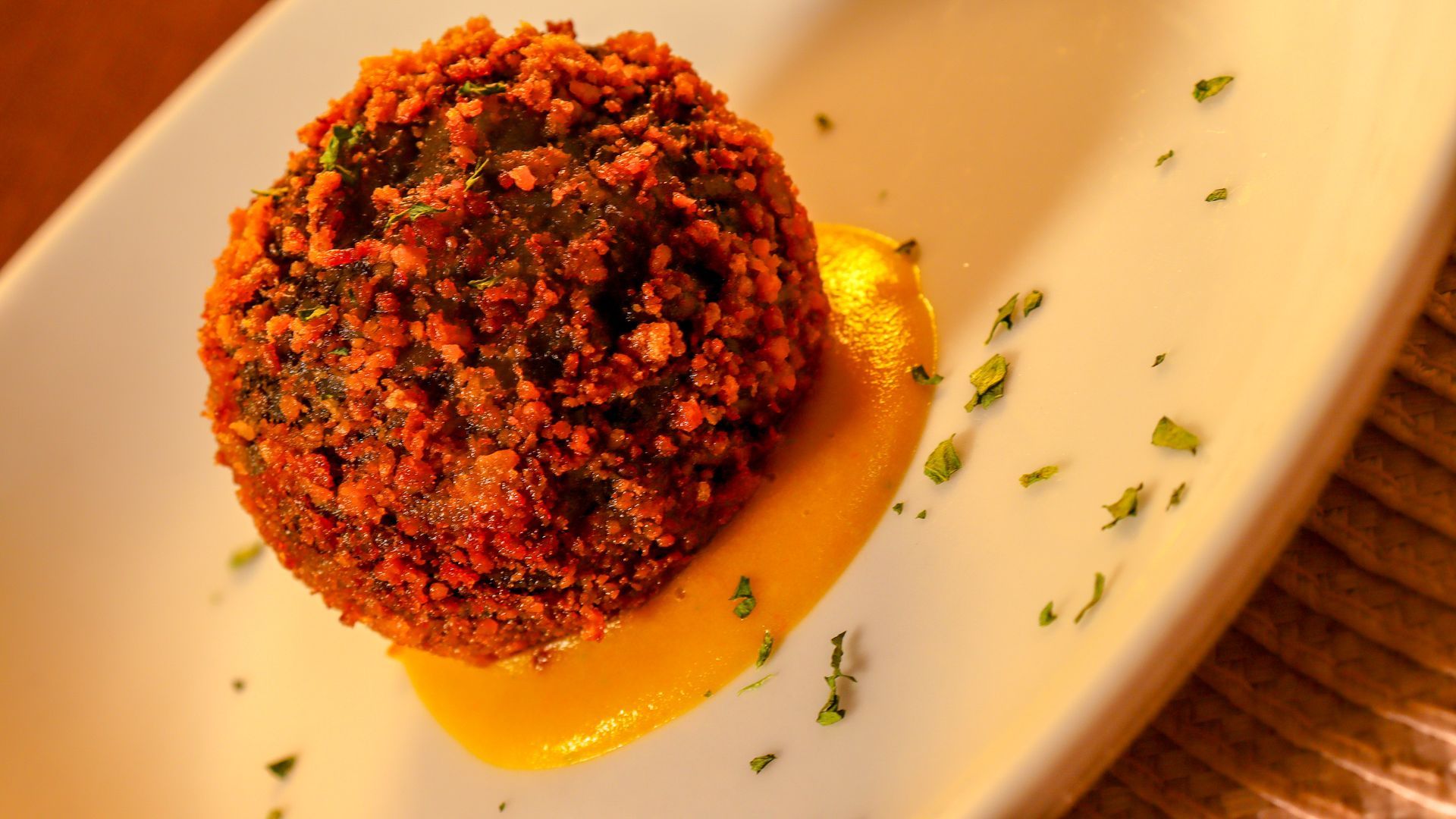 Un piatto elegante con un fritto di pesce poggiato su una salsa e circondato da odori scelti ad hoc