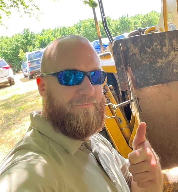 A man with a beard wearing sunglasses is giving a thumbs up